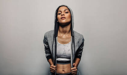 Fit Frau trägt einen Hoodie Sportbekleidung. Weibliche Fitness-Modell posiert in Sportkleidung gegen grauen Hintergrund. - JLPSF00272
