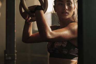 Muskulöse Frau hält Gymnastikringe im Fitnessstudio und schaut weg. Starke Frau, die sich nach dem Training ausruht. - JLPSF00291