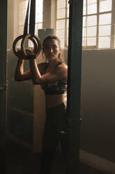 Fit woman working out on gymnast rings at the gym. Young female exercising at gym. - JLPSF00292