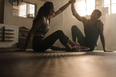 Fit man and woman sitting on floor and high fiving at the gym. Fitness couple after successful workout session in gym. - JLPSF00298