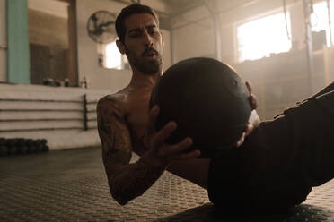 Ein Sportler trainiert mit einem Fitnessball im Fitnessstudio. Ein männlicher Sportler macht eine Bauchmuskelübung im Fitnessstudio. - JLPSF00320