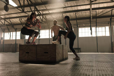 Eine Gruppe von Menschen springt auf Holzkisten in einem Fitnessstudio. Drei Menschen machen Box Jumping Workout im Fitnessstudio. - JLPSF00324