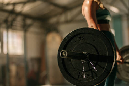 Frau beim Training mit schweren Gewichten im Fitnessstudio. Fokus auf schwere Langhantel in den Händen einer Sportlerin. - JLPSF00328