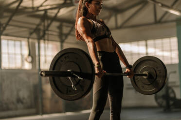 Determined and strong fitness woman training with heavy weights in fitness club. Female athlete holding heavy weight barbell in gym. - JLPSF00332