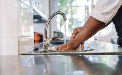 Nahaufnahme eines Kochs, der sich die Hände in einer Großküche wäscht. Ein Mann wäscht sich die Hände in einem Waschbecken mit Leitungswasser. - JLPSF00338