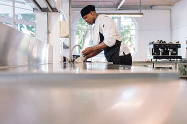 Ein Restaurantangestellter tränkt ein Tuch in Wasser, um die Theke zu reinigen. Ein Mann arbeitet in einer Großküche. - JLPSF00340