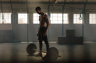 Mann trainiert mit Langhantel im Fitnessstudio. Mann steht mit schweren Gewichten Langhantel auf Turnhallenboden. - JLPSF00342