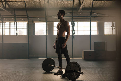Muskulöser junger Mann mit Langhantel im Fitnessstudio. Mann steht mit schweren Gewichten auf dem Boden des Fitnessstudios. - JLPSF00343