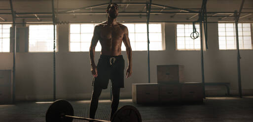 Young man with muscular body standing in the gym with heavy weights. Sportsman at crossing training gym with barbell on floor. - JLPSF00346