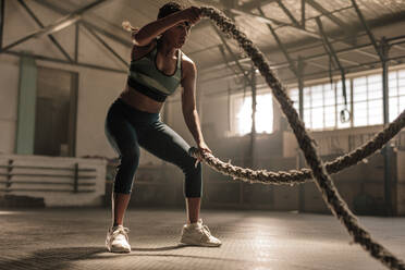 Fitness woman using training ropes for exercise at gym. Athlete working out with battle ropes at cross gym. - JLPSF00359