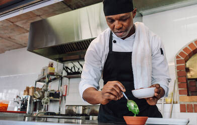 Männlicher Koch bei der Zubereitung von Soße in einer Restaurantküche. Afrikanischer männlicher Gourmetkoch bei der Arbeit in einer Großküche. - JLPSF00360