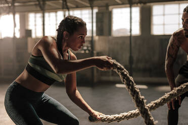 Kräftige, muskulöse Frau trainiert mit Battle Rope im Fitnessstudio mit Personal Trainer. Battle Rope Workout im Fitnessstudio mit Trainer. - JLPSF00365