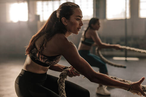 Zwei junge Frauen machen Übungen mit dem Seil in einem Fitnessstudio. Fitness Frauen ziehen Seil im Fitnessstudio. - JLPSF00381