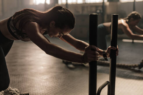 Starke junge Frau schiebt den Schlitten im Fitnessstudio. Frauen machen intensives körperliches Training im Fitnessstudio. - JLPSF00382