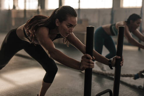 Starke junge Frau, die das Prowler-Fitnessgerät schiebt. Fitte Frauen, die im Fitnessstudio trainieren. - JLPSF00384