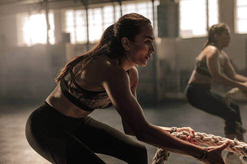 Zwei junge Frauen machen Übungen mit Seilen in einem Fitnessstudio. - JLPSF00387