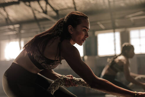 Zwei junge Frauen machen Seilübungen in einem Fitnessstudio. Fitness-Frauen ziehen ein schweres Seil in einem Cross-Trainingsstudio. - JLPSF00389