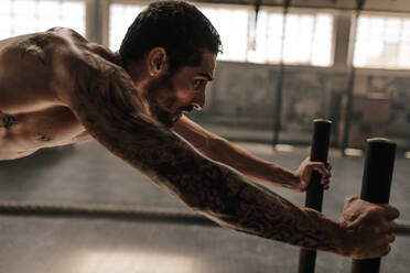 Starker junger Mann beim Schieben des Schlittens im Fitnessstudio. Muskulöser männlicher Athlet bei intensivem körperlichen Training im Fitnessstudio. - JLPSF00390