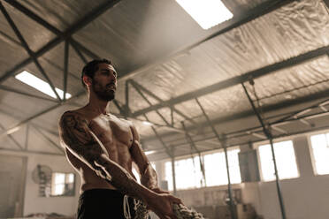 Muscular man exercising with heavy rope at health club. Fitness male pulling rope at gym. - JLPSF00396