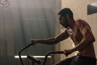 Fit young man using exercise bike at the gym. Fitness male using air bike for cardio workout at cross training gym. - JLPSF00402