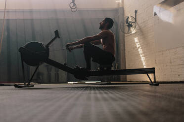 Muscular male using rowing machine in gym. Fit man doing workout in fitness club. - JLPSF00410