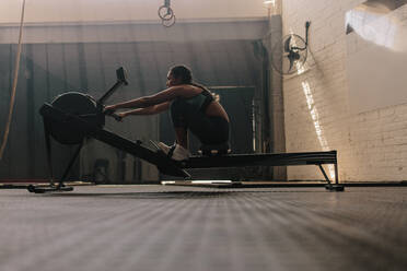 Weibliche Athletin auf dem Rudergerät, fitte Frau beim Cardio-Training im Fitnessstudio. - JLPSF00413