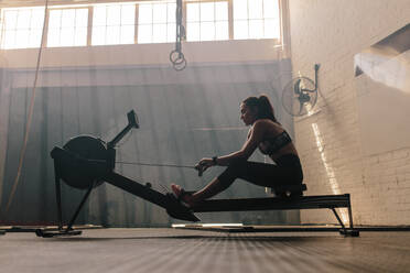 Fitte junge Frau, die im Fitnessstudio auf einem Rudergerät trainiert. Frau beim Ausdauertraining im Fitnessclub. - JLPSF00415