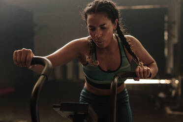 Fit young woman using exercise bike at the gym. Fitness female using air bike for cardio workout at gym. - JLPSF00429