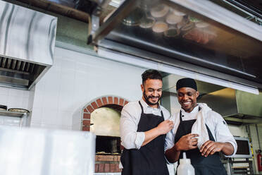Lächelnde professionelle Köche arbeiten in der Restaurantküche. Glückliche Köche in Uniform und Schürze in der Großküche. - JLPSF00436