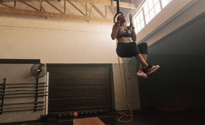 Eine fitte Frau benutzt Gymnastikringe als Teil eines Cross-Trainings im Fitnessstudio. Eine muskulöse junge Sportlerin trainiert mit Ringen. - JLPSF00437