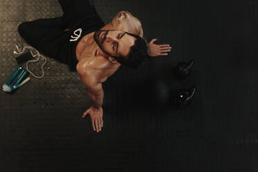 Aufnahme von oben eines erschöpften Mannes, der sich nach dem Training im Fitnessstudio ausruht. Ein muskulöser Mann, der nach einem intensiven Training eine Pause einlegt. - JLPSF00441
