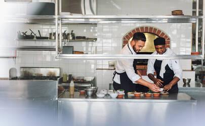 Professionelle Köche arbeiten in einer Großküche und bereiten gemeinsam ein Gericht zu. Köche kochen in einer Großküche. - JLPSF00447