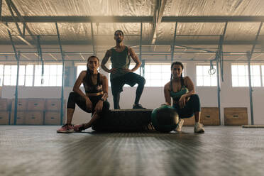 Porträt von drei jungen Leuten, die sich nach dem Training im Fitnessstudio ausruhen und in die Kamera schauen. Kleine Gruppe von Menschen nach dem Training im Fitnessstudio. - JLPSF00451