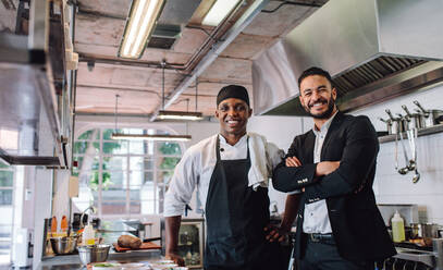 Porträt eines Restaurantbesitzers mit Koch in der Küche. Geschäftsmann und professioneller Koch stehen zusammen und schauen in die Kamera. - JLPSF00454