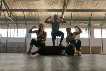 Young people posing and flexing their muscles in gym. Group of people at gym showing their muscular biceps and smiling. - JLPSF00455