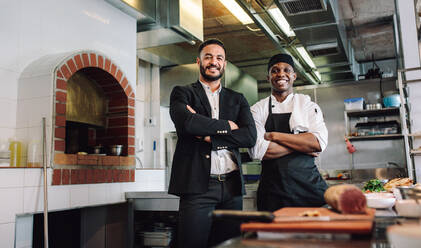 Porträt eines Restaurantleiters mit Koch in der Küche. Geschäftsmann und professioneller Koch stehen zusammen und schauen in die Kamera. - JLPSF00457