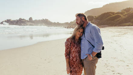 Romantisches reifes Paar, das sich am Meer umarmt. Liebevoller älterer männlicher Fotograf, der sich mit seiner Frau am Strand umarmt. - JLPSF00473