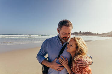 Porträt eines romantischen reifen Paares, das Zeit miteinander am Strand verbringt. Glücklicher älterer Mann, der sich mit seiner Frau am Meeresufer umarmt. - JLPSF00474