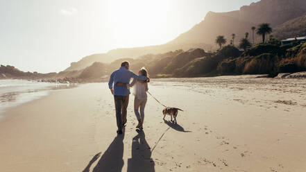 Älteres Paar, das mit seinem Hund am Strand spazieren geht. Rückansicht eines liebenden reifen Paares am Strand mit Hund. - JLPSF00475