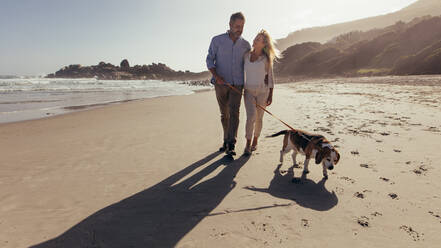Ganzaufnahme eines älteren Paares, das morgens mit seinem Hund am Strand spazieren geht. Älteres Paar beim Morgenspaziergang mit seinem Hund. - JLPSF00476