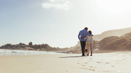 Romantisches Paar, das mit einem Hund am Strand spazieren geht. Liebendes reifes Paar, das mit einem Hund am Meer spazieren geht. - JLPSF00479