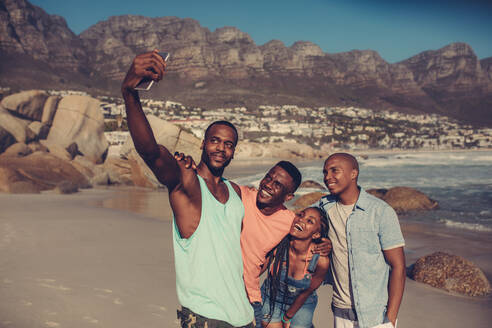 Eine Gruppe von Freunden macht ein Selfie am Strand. Die besten Freunde stehen an der felsigen Küste und machen ein Selbstporträt mit dem Smartphone. - JLPSF00492