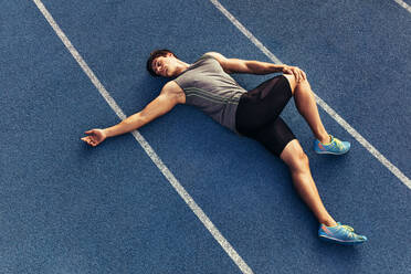 Athlete doing stretching exercises on the running track. Runner stretching muscles by lying on the track. - JLPSF00510