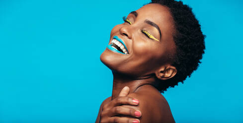 Close up von fröhlichen jungen Frau mit bunten Make-up. Beauty-Porträt von weiblichen Modell mit lebendigen Make-up lachen auf blauem Hintergrund. - JLPSF00536