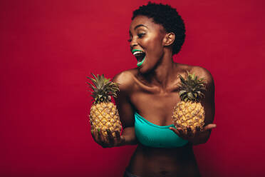 Schwarze Frau mit Ananas in der Hand, lachendes weibliches Modemodell vor rotem Hintergrund. - JLPSF00543