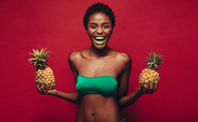 Lachende junge afrikanische Frau mit Ananas in der Hand. Weibliches Model mit Ananas lachend auf rotem Hintergrund. - JLPSF00545