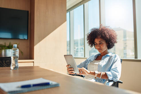 Indoor shot of young african woman sitting in office and using digital tablet. Creative businesswoman using tablet pc. - JLPSF00555