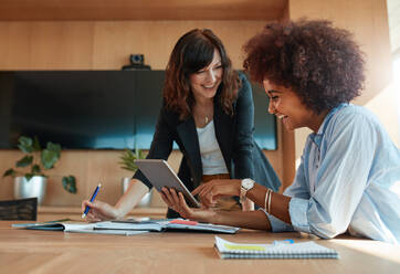 Aufnahme von zwei jungen Frauen, die gemeinsam an einem digitalen Tablet arbeiten. Kreative weibliche Führungskräfte, die sich in einem Büro treffen, einen Tablet-PC benutzen und lächeln. - JLPSF00557