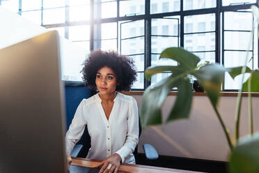 Innenaufnahme einer jungen afrikanischen Frau, die an ihrem Schreibtisch sitzt und am Computer arbeitet. Eine weibliche Führungskraft arbeitet im Büro. - JLPSF00601