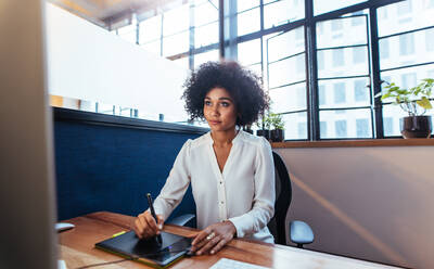 Junge weibliche Grafikdesignerin arbeitet am Computer mit Zeichenblock im Büro. Junge afrikanische Frau mit digitalem Grafiktablett und Zeichenstift für neues Projekt. - JLPSF00602